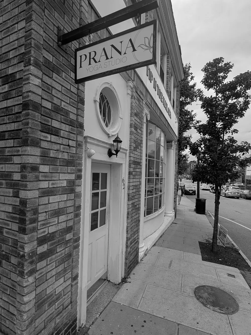 The Prana Yoga Studio sign hanging above the white entrance door at 62 Main Street, with the number 62 on the door frame.