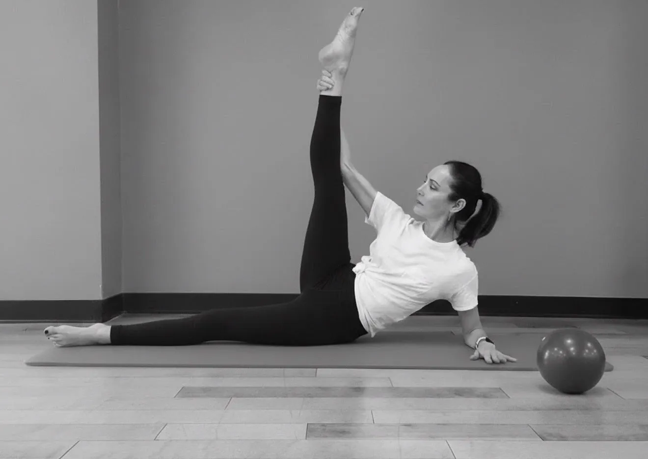 Jennifer Pagoto on a Pilates mat, propped on one arm with one leg raised straight up, a mini stability ball beside her.